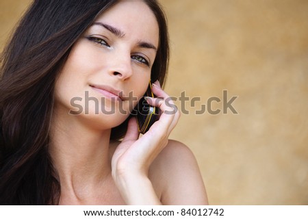 Close-up portrait of young attractive brunette woman speaking on mobile phone against yellow background.