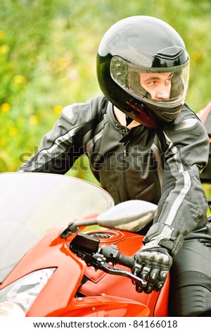 Portrait of young man wearing helmet, leather costume, driving red motorbike.