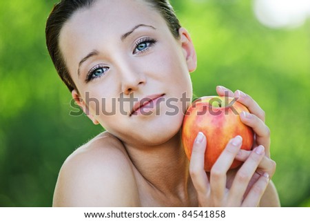 Close-up portrait of beautiful brunette woman holding red apple at summer green park.