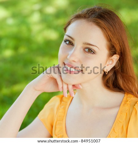 A beautiful girl is sitting on a park bench on a background of green nature - stock photo