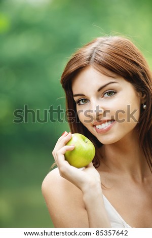Portrait of young lovely brunette woman holding juicy fresh delicious apple at summer green park.