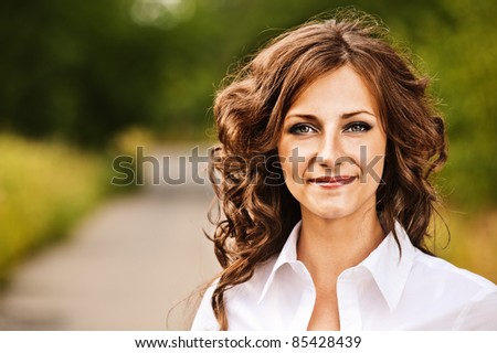 Portrait of beautiful young brunette woman wearing white blouse at summer green park.