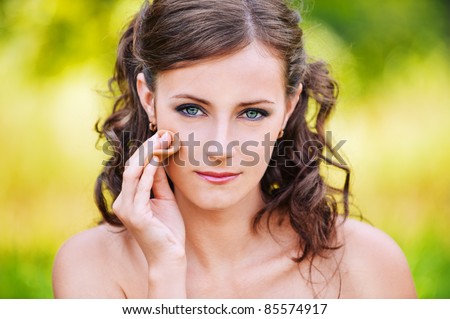 Close-up portrait of serious dark-haired woman making herself up with powder and sponge at summer green park.