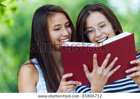 Two women are cheerful beautiful young in the summer the park are holding red book, read