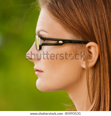 Beautiful young smiling woman in white blouse and glasses, profile close up, on green background of city park.