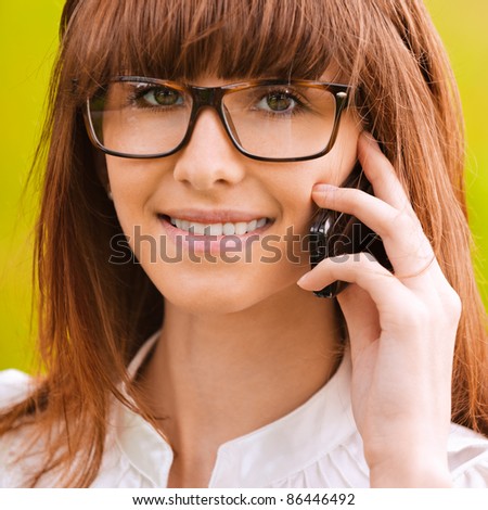 Close-up portrait of young beautiful smiling woman speaking on telephone at park.