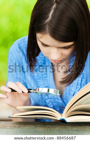 portrait young woman short hair close-up reading book magnifier background summer green park