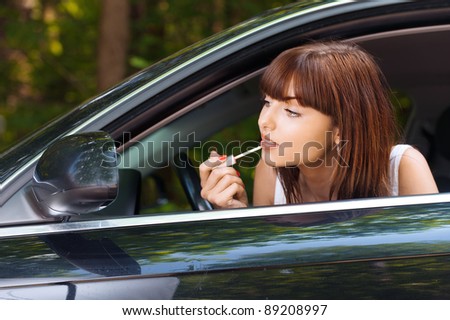 Portrait beautiful young woman sitting car peeps head out window looking mirror paints lips
