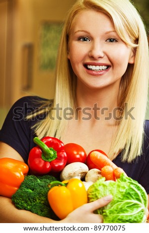 portrait of a beautiful young smiling woman holding a lot of vegetables (peppers, cabbage, tomatoes, mushrooms, carrots, cauliflower)