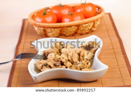 Close-up on bamboo table cloth dish with braised chicken and wicker basket with red tomatoes