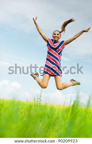 young, attractive woman in striped dress jumps up against the blue sky with clouds and green fields