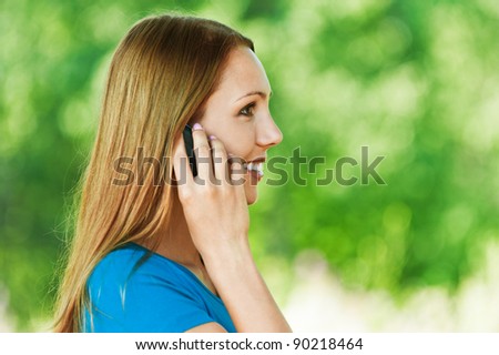 young, attractive woman in profile, said by cell phone, smiling background summer green park