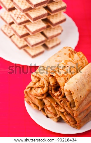 plate of fried pancake-wrapped rolls and plate of waffles lined tower-two plates with high-calorie treats on red tablecloth