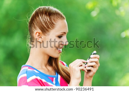portrait of pretty woman in profile, holds mobile phone on background summer green park