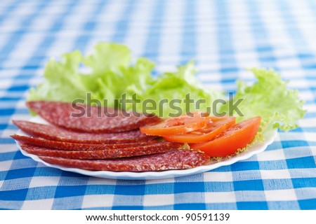 white plate (sliced ??salami sausage, lettuce, sliced ??tomato) background tablecloth blue cell
