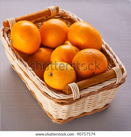 close-up of lot of juicy, ripe oranges (Mandarin) in wicker basket on the table with cloth background