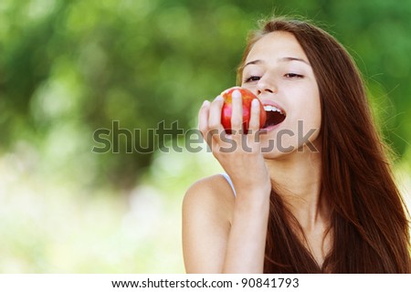 pretty young woman long black hair Park biting red apple