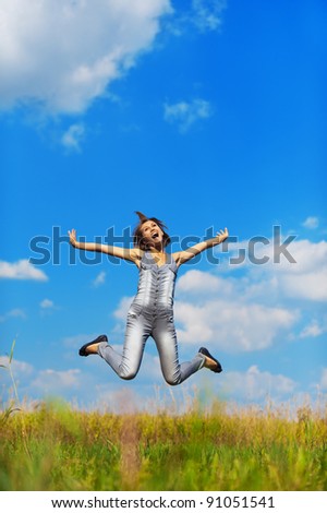 fun, young, slender girl jumps up on background of meadows and sky with clouds