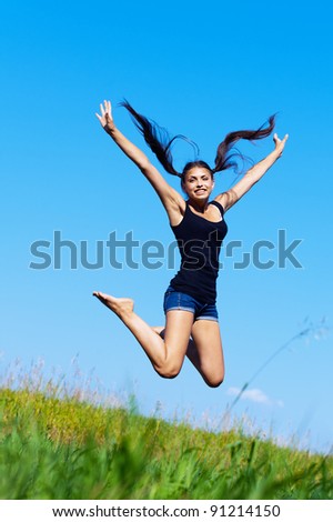 funny, beautiful, young woman jumps up on the background of green grass and blue sky