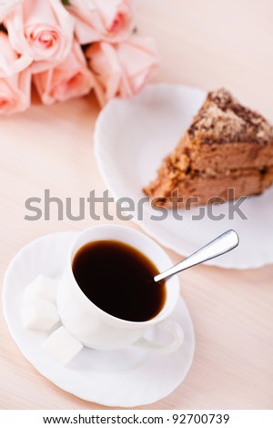 cup of black coffee on saucer strong with three pieces of sugar and slice of chocolate sponge cake on plate next to bouquet of five roses on pink table