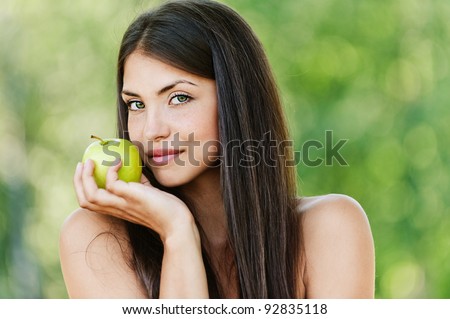 long-haired young woman with bare shoulders holding green apple background summer green park