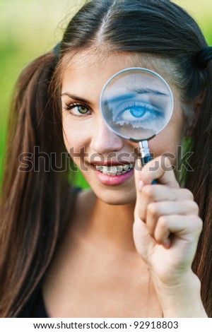 portrait of young, pretty, long-haired girl holding magnifying glass near the eye