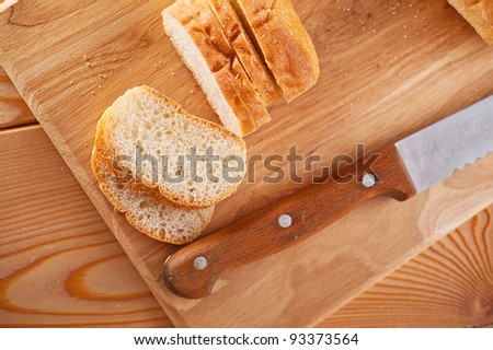 Close-up sliced ??bread (long loaf) on cutting wooden board, knife