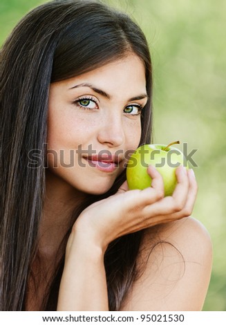 long-haired young woman with bare shoulders holding green apple background summer green park