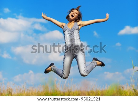 fun, young, slender girl jumps up on background of meadows and sky with clouds