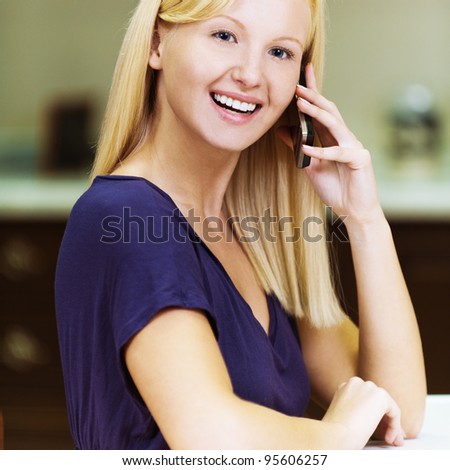 blonde pretty girl smiling talking on a cell phone while sitting at kitchen table
