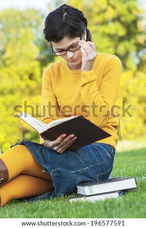 Young student holding books on autumn background.