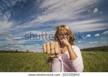 young beautiful woman beats fist towards to camera against nature