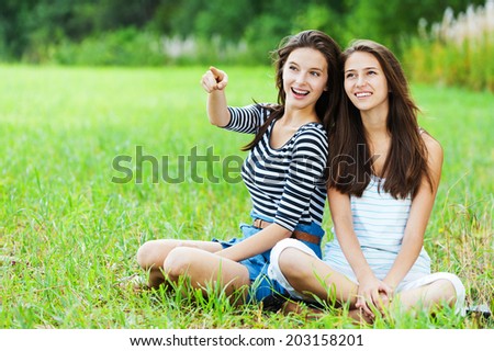 two sisters girlfriends long dark hair sitting cross-legged grass park talking