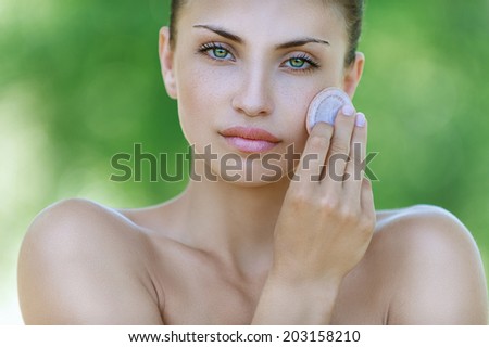 Beautiful dark-haired calm young woman handles face creams, against background of summer green park.