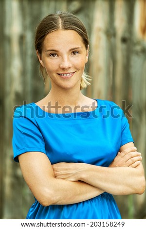 Portrait of dark-haired beautiful young woman in blue blouse, against background wooden fence