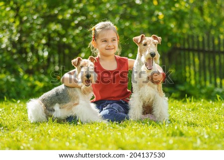 Little girl with two dogs of breed fox terrier on green lawn