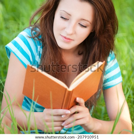 Portrait of beautiful young woman sits on grass and reading book at summer green park
