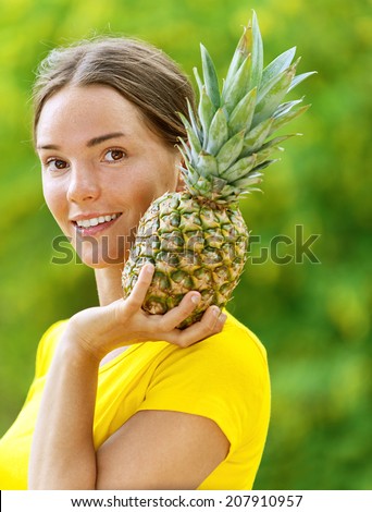 Portrait of dark-haired smiling beautiful young woman in yellow blouse with pineapple, against green of summer park.