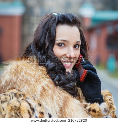 Young smiling beautiful woman in brown coat with fur collar talking on mobile phone.