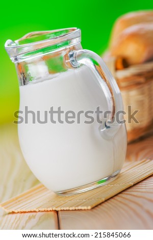 on wooden table pone bun, pitcher of milk,on green background