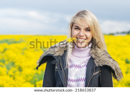 Young beautiful woman holds in teeth a yellow floret against meadow and the sky