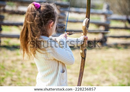 Beautiful little girl shoots bow at entertainment park.
