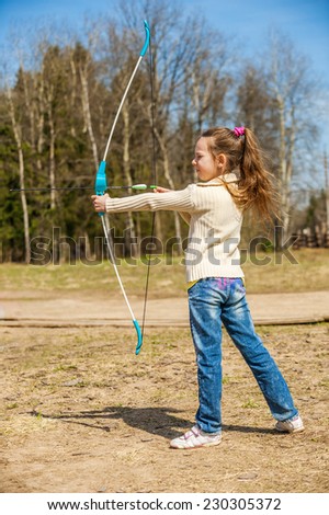 Beautiful little girl shoots bow at entertainment park.