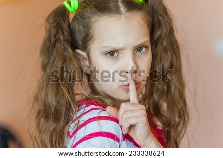 Little beautiful girl frowned and calls for silence, putting finger to his lips.