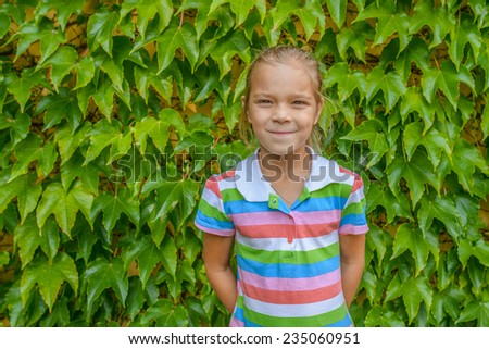 Beautiful little cheerful girl on background of fallen wall of wild grapes.