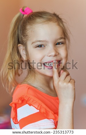 Little beautiful girl in red dress laughs and puts his finger to lips.