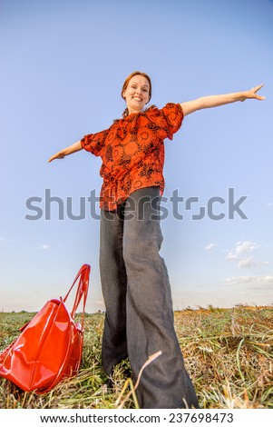 Young beautiful woman with red bag standing in field.