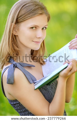 portrait of beautiful young blond woman reading book in summer green park