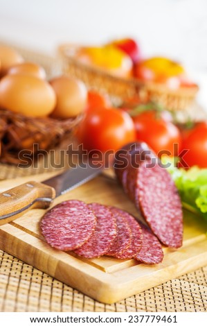 foods (tomatoes, eggs, apples, Bulgarian pepper, hazelnuts, garlic and smoked sausage on cutting board with knife) on tablecloth