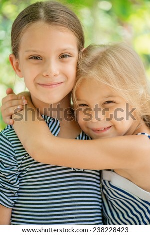 Two young sisters hugging, in summer city park.